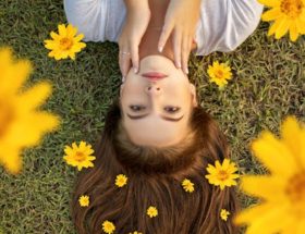 Upside down portrait of a woman lying on grass with yellow flowers in her hair.