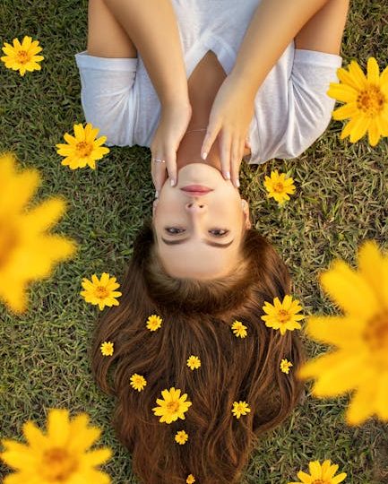 Upside down portrait of a woman lying on grass with yellow flowers in her hair.